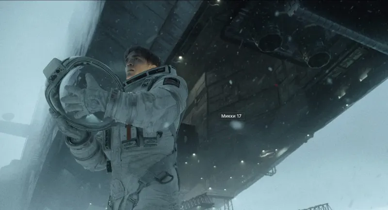 Роберт Паттинсон в футуристическом рабочем комбинезоне смотрит в камеру